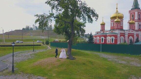 新娘和新郎在教堂鸟瞰图的树旁跳舞