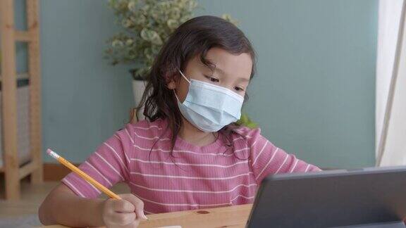 一个亚洲小女孩戴着医用口罩在笔记本电脑上通过网络家教在线学习