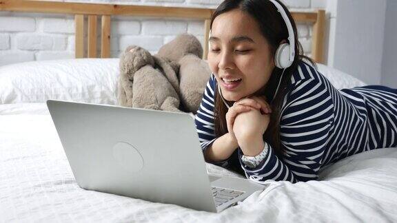 年轻女子躺在床上用手提电脑进行视频通话耳机视频会议