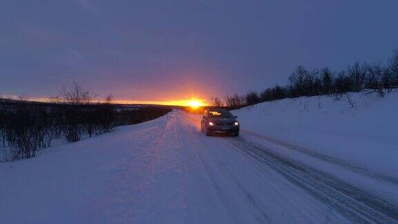 近距离观察:汽车在冰雪覆盖的森林道路上行驶在下雪的金色冬季日落