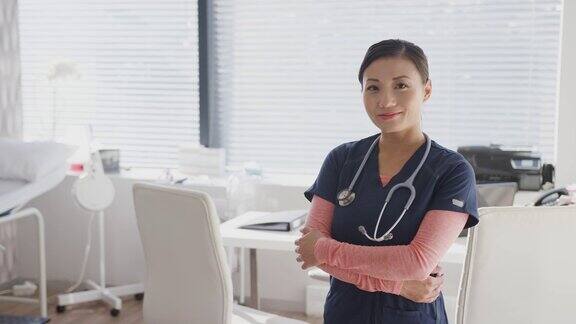 微笑的女医生穿着手术服听诊器站在办公室的办公桌旁