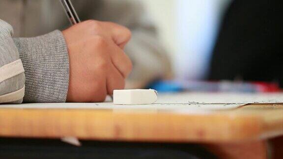 学校大学的学生手拿考试用铅笔写在光学形式的答卷上在课桌上做期末考试教育评估