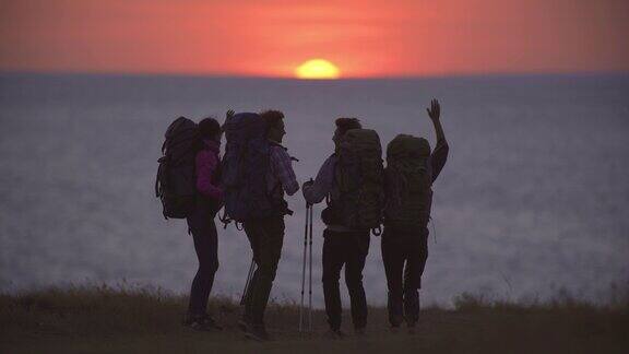 在夕阳的背景下四个旅行者走到海边