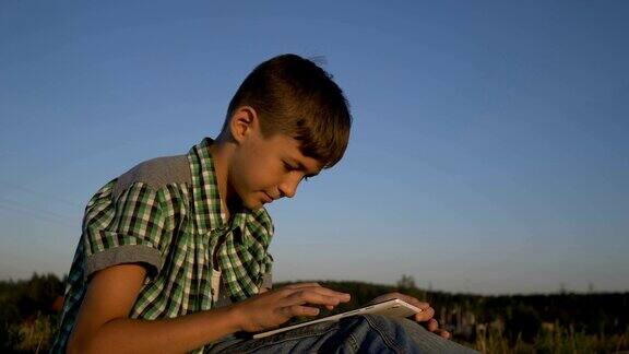 日落时分男孩坐在田野里用平板电脑