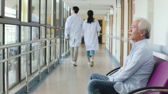 年长的亚洲人坐在医院走廊上看起来悲伤和崩溃