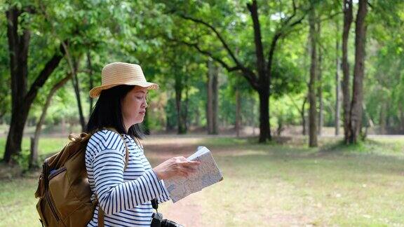 亚洲女性背包旅行者在森林旅行时使用地图和拍照节日假期旅行的生活方式