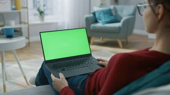 坐在沙发上的年轻女子用绿色模拟屏幕的笔记本电脑工作女孩使用电脑上网浏览看内容在社交网络聊天