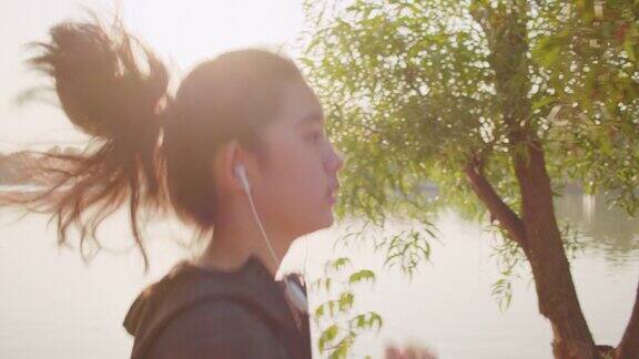 中镜头:迷人的亚洲少女听音乐同时在公园的湖上奔跑年轻女子晨跑锻炼