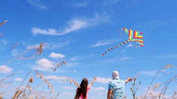 幸福的家庭爸爸和女儿放着五颜六色的风筝站在一个带着小穗的田野里映衬着蓝天阳光明媚的夏天