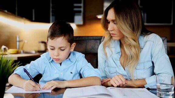 母亲微笑着帮儿子做作业口述着课文坐在餐桌旁帮你写字