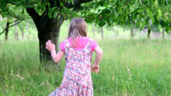 一个可爱的女孩在自然花园里跳舞小女孩在小蹦床上又跳又跳小女孩穿着花裙子戴着白色的帽子