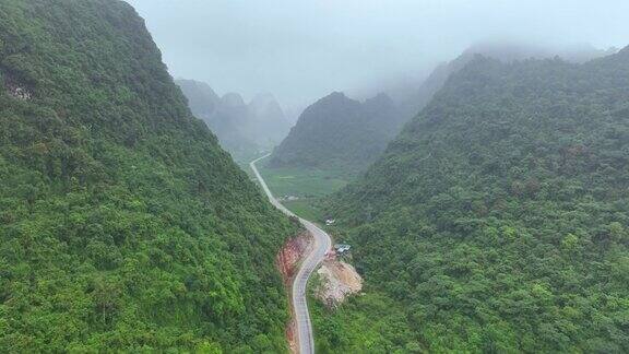 无人机在雾蒙蒙的热带雨林附近蜿蜒的山路上飞行电影镜头鸟瞰宏伟的热带山脉景观在越南北部