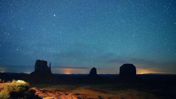 星星和流星的时间流逝在夜空与岩石的轮廓在远处在犹他州亚利桑那州的纪念碑谷沙漠在晚上
