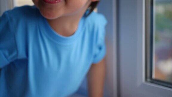 快乐的孩子穿着蓝色t恤和紧身衣坐在窗台上