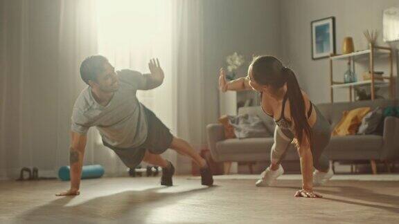 一个强壮美丽的运动健身夫妇穿着运动服在明亮宽敞的客厅里做俯卧撑和互相击掌的慢动作镜头