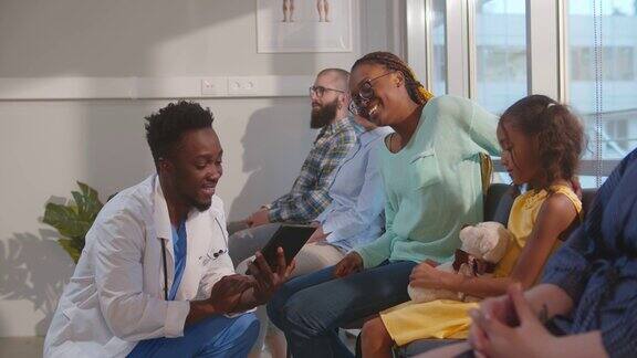 非裔美国男医生在医院候诊室与母亲和孩子交谈