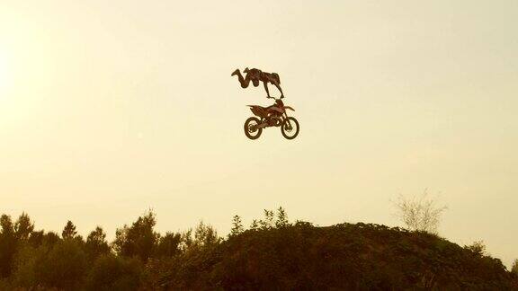 慢动作:极端专业的摩托车越野赛车手跳过尘土飞扬的大空气踢过太阳