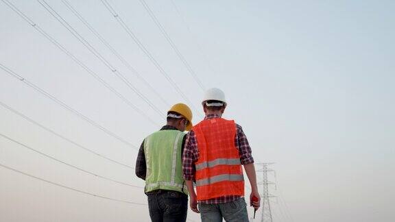 两个电气工程师在日落的背景下讨论高压输电塔