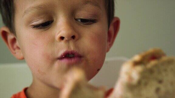 一个可爱的6岁白人男孩向镜头展示了他的三明治上的咬痕然后又咬了一口笑了
