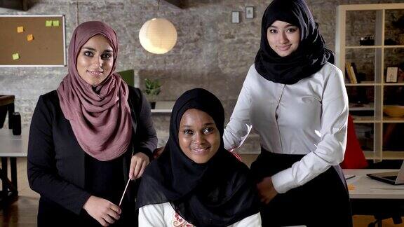 三名年轻的穆斯林妇女戴着头巾在现代办公室里微笑着看着镜头黑人穆斯林妇女和同事一起工作