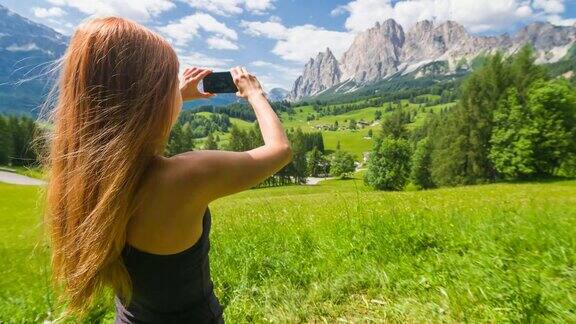 女游客欣赏山的景色在温暖的晴天用智能手机拍照