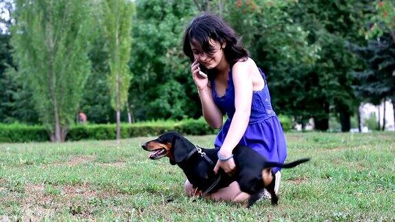女孩和她的宠物腊肠狗在公园里打电话