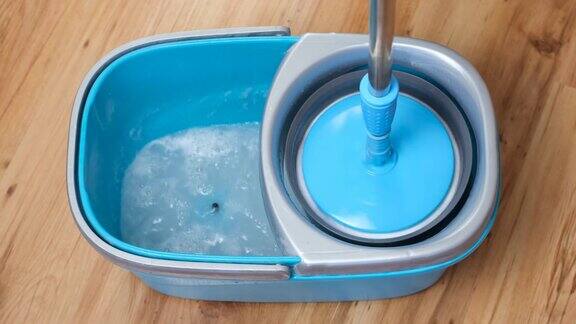 在装满水和洗涤剂的蓝色桶中清洗和旋转拖把伸缩手柄