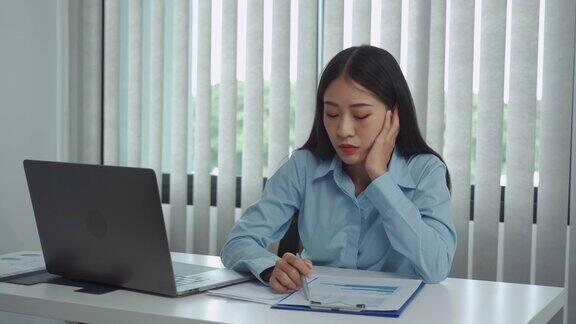 年轻的亚洲女性对工作感到厌烦觉得在下午处理笔记本电脑上的数据很懒