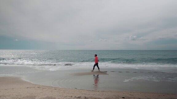 苗条的女性在沙滩上沿着海浪行走漂亮女人在海边冲浪海浪溅起水花产生泡沫暑假女游客海洋的微风