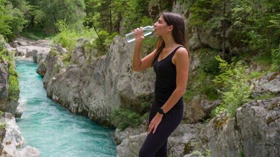 开朗的女游客在山间小溪边欣赏美景喝着水
