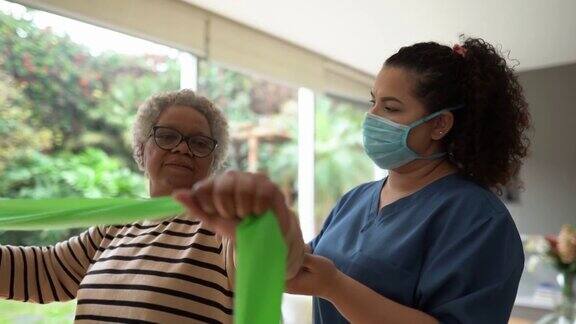 老年妇女在物理治疗师的支持下戴着防护口罩用阻力带做运动