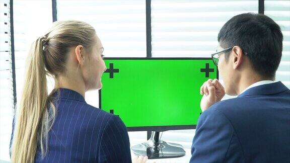 两个商务人士正在用绿色屏幕的笔记本电脑交谈