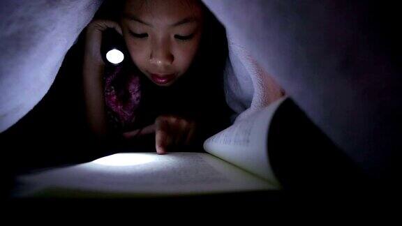 一个亚洲女孩用手电筒在床上看书