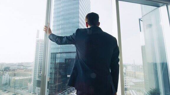 西装革履的商人站在他的办公室里看着窗外思考着下一个大的商业合同主要城市商务区全景窗口蓝色的颜色