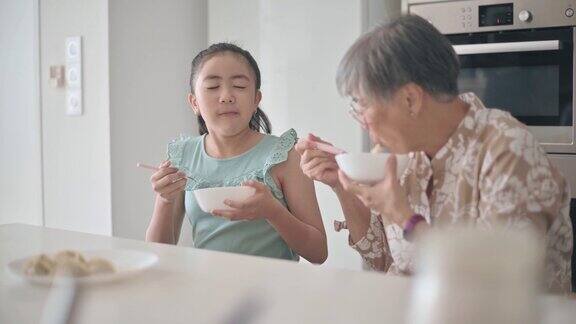 亚洲华裔孙女和她的祖母在厨房的柜台吃饺子