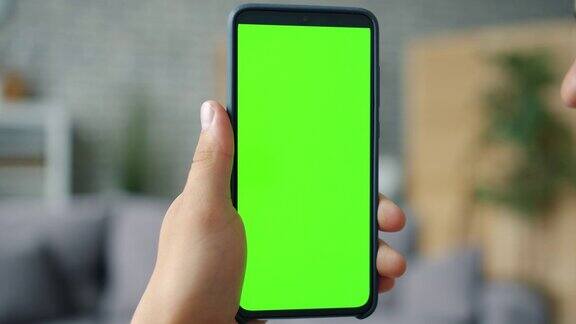 男性手握色度键绿色屏幕智能手机在公寓的特写