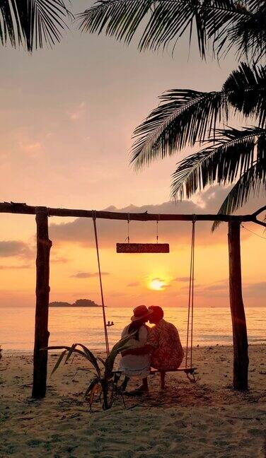 日落时分一对男女在泰国长岛的海滩上荡秋千