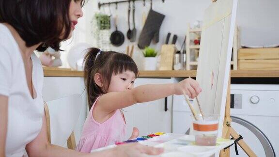 亚洲年轻快乐的女儿和妈妈在画板上画画快乐的家庭活动小女孩学习如何用水彩画和画笔画画享受与妈妈的创造力