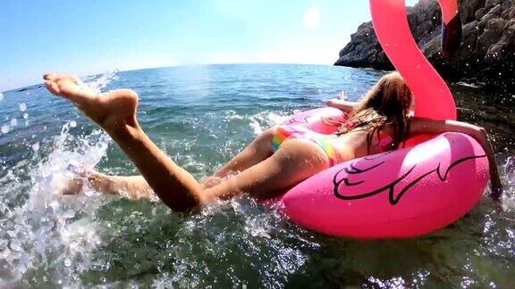 年轻苗条的女子享受大海和太阳躺在一个充气的粉红色火烈鸟