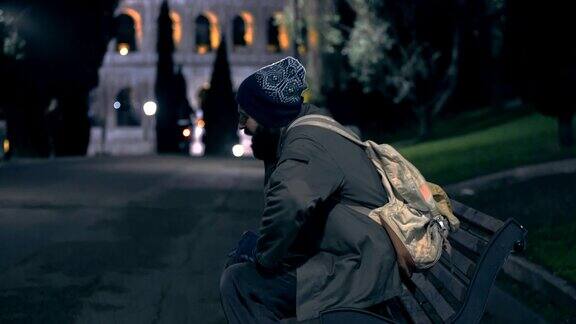 孤独的无家可归者晚上坐在长凳上检查他的施舍