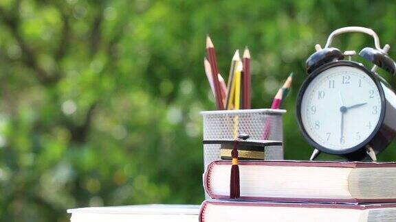 毕业或教育知识留学理念:毕业帽在课本上铅笔盒和书桌上的时钟模糊的绿光背景回到学校