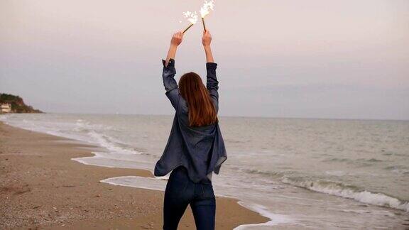 年轻迷人的女人在日落时在海边跑步的背影双手拿着燃烧的闪闪发光的蜡烛Slowmotion拍摄