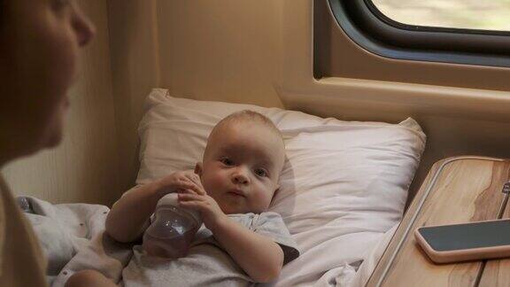 母子俩乘火车旅行火车车厢里6个月大的可爱男婴在靠窗的座位上喝奶瓶里的奶