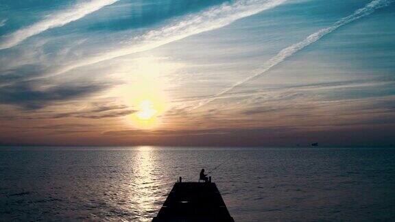 人在码头上钓鱼在美丽的日出剪影