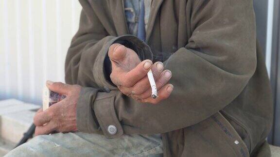 在户外吸烟的流浪汉特写乞丐的手拿着一根香烟
