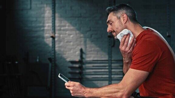 4k视频记录了一个英俊成熟的男人在健身后独自坐在健身房使用手机