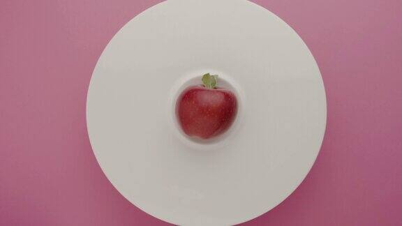 苹果顶构图与极简主义白色盘子拍摄在粉红色的背景