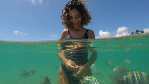 在热带海滩上喂鱼的年轻女子