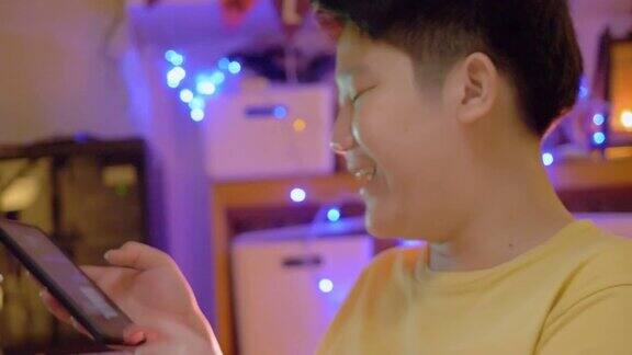 亚洲男孩晚上在家玩手机游戏背景是圣诞灯光