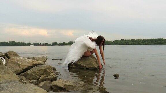 河上的一块巨石上一个年轻美丽的女人站在白色翅膀的天使形象中